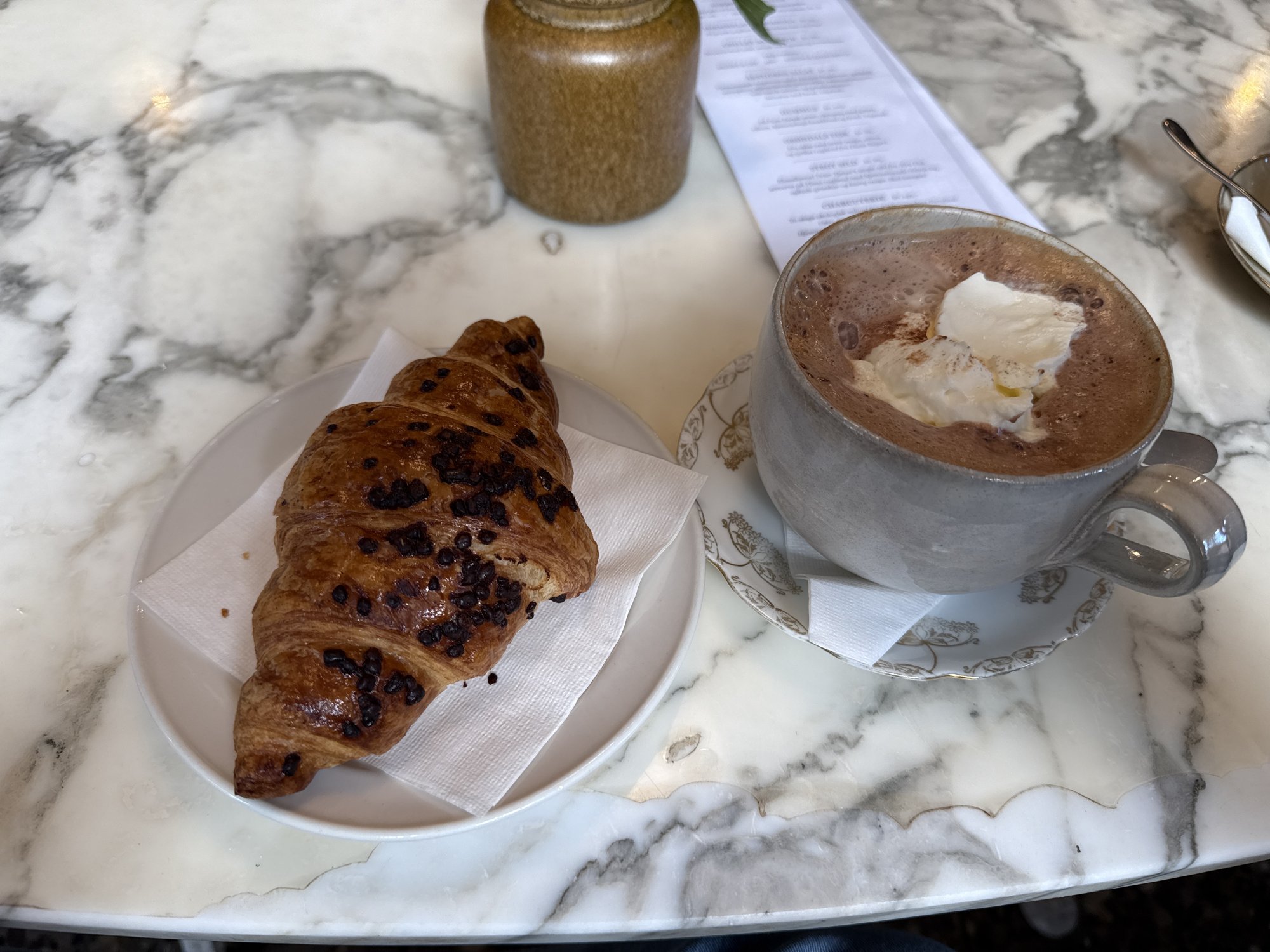 Heiße Schokolade mit Sahne und ein Schokocroissant auf einem Marmortisch