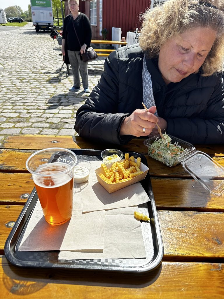 Tanja am Holztisch vor der Räucherei mit Tablett, Pommes und Bier