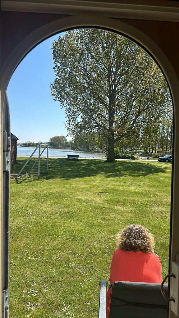 Blick aus Emmas Fenster auf die Wiese am Stellplatz, Tanja im roten Campingstuhl