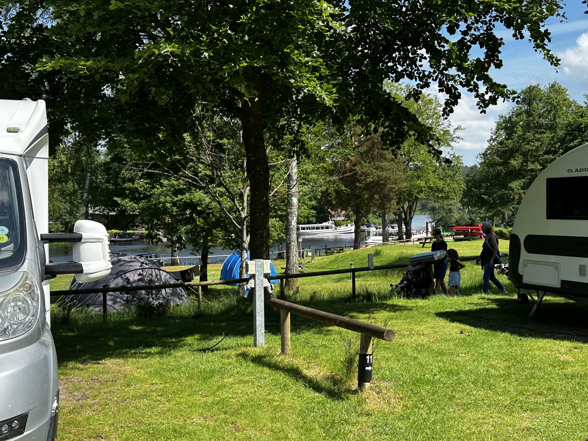 Blick über die Zeltwiese zum Wasser, ein Ausflugsschiff fährt vorbei