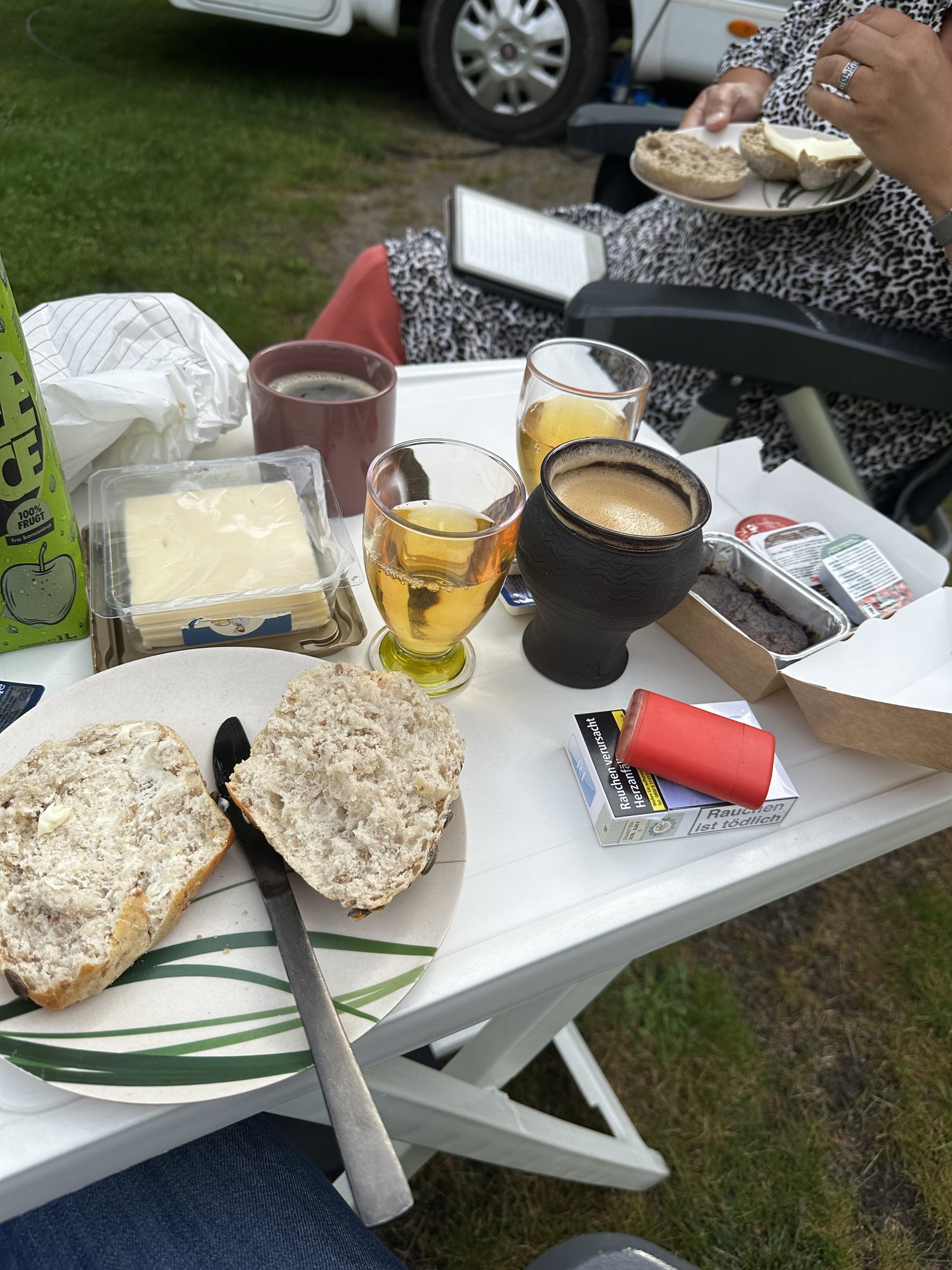 Frühstückspaket mit Körnerbrötchen, Butter, Käse und Kaffee am Campingtisch