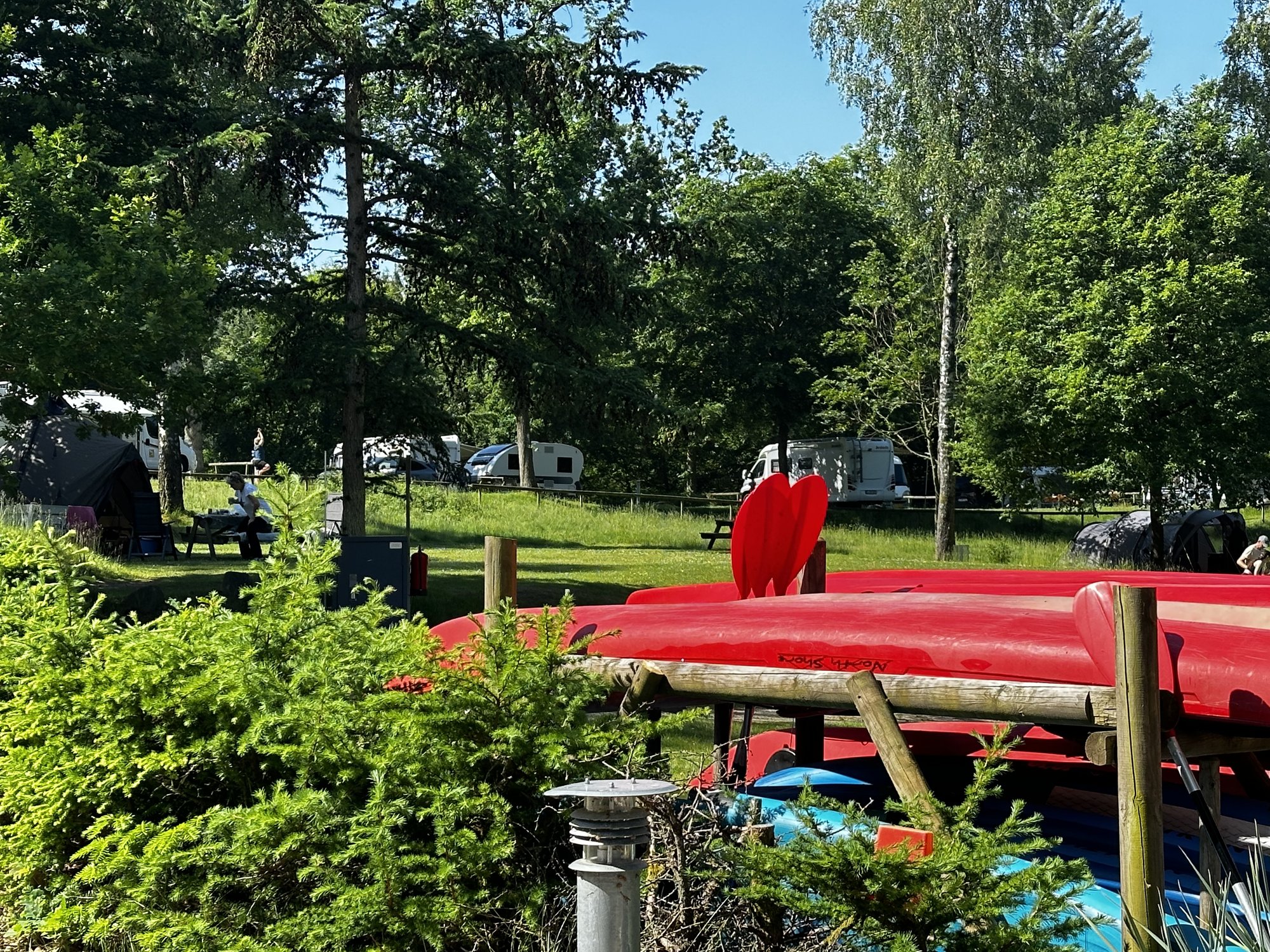 Gestapelte rote Kanus und SUP-Bretter am Rand der Campingwiese