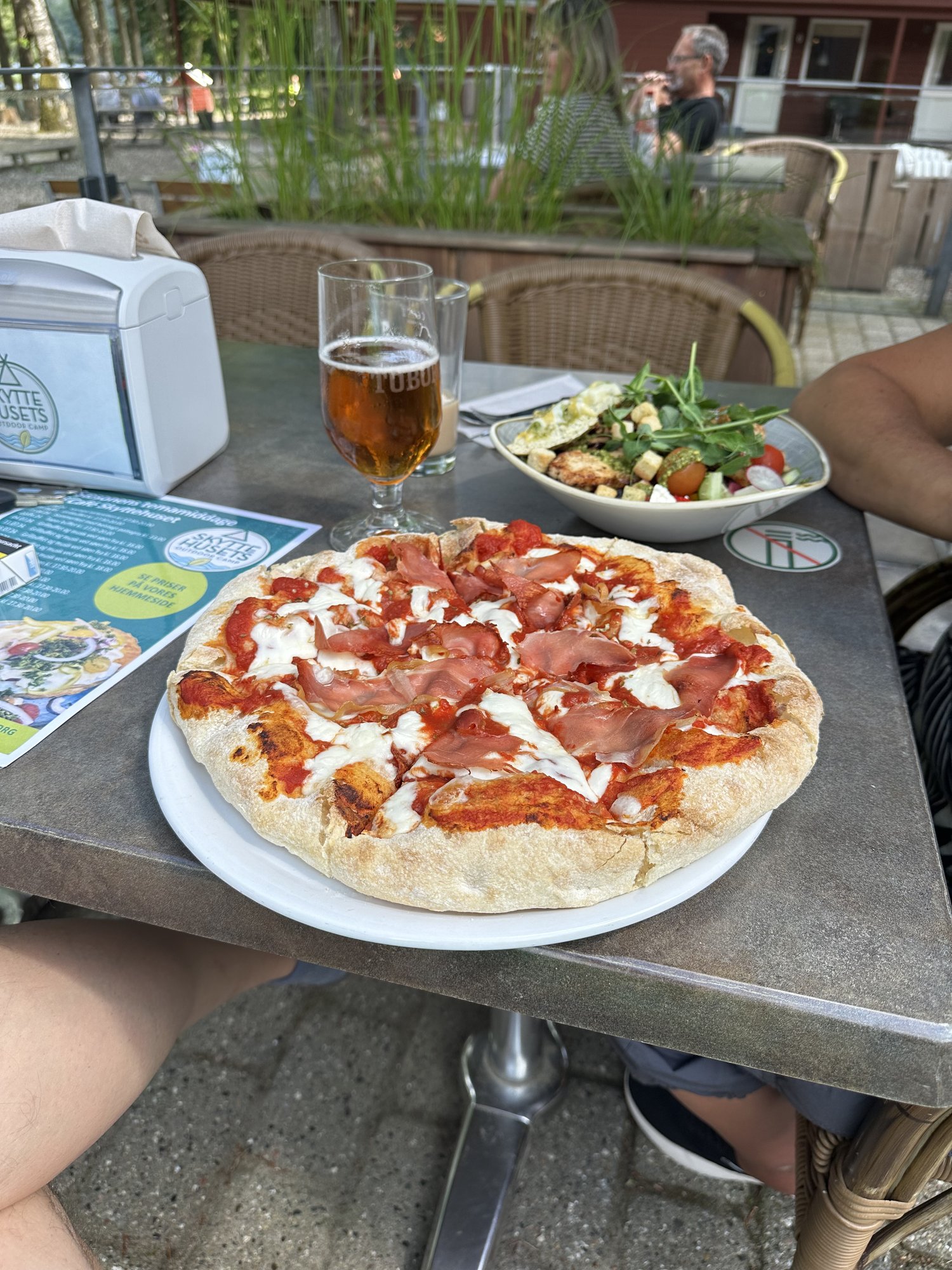 Pizza mit Prosciutto und Mozzarella, dazu Salat und ein Bier
